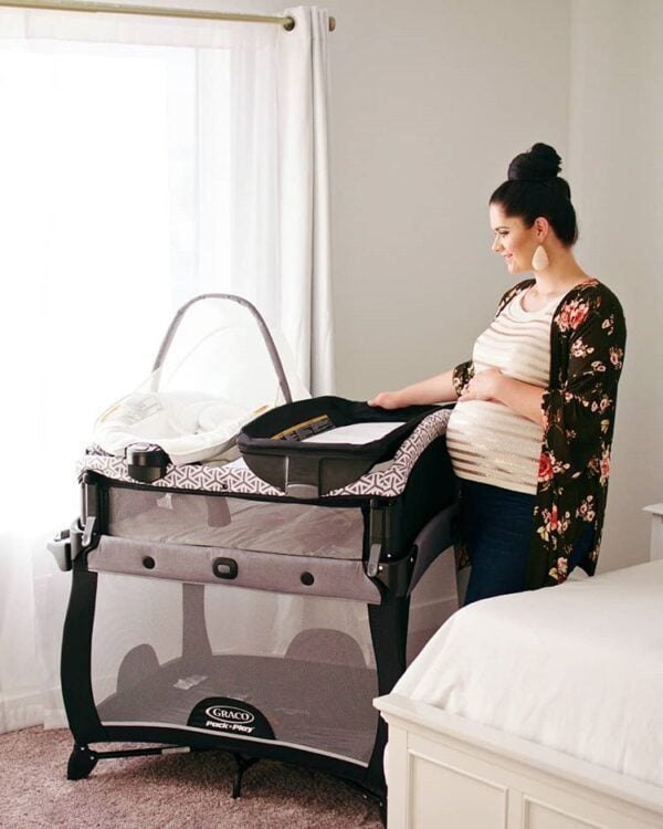 Mom stands by a Graco pack 'n play and holds her baby belly. 