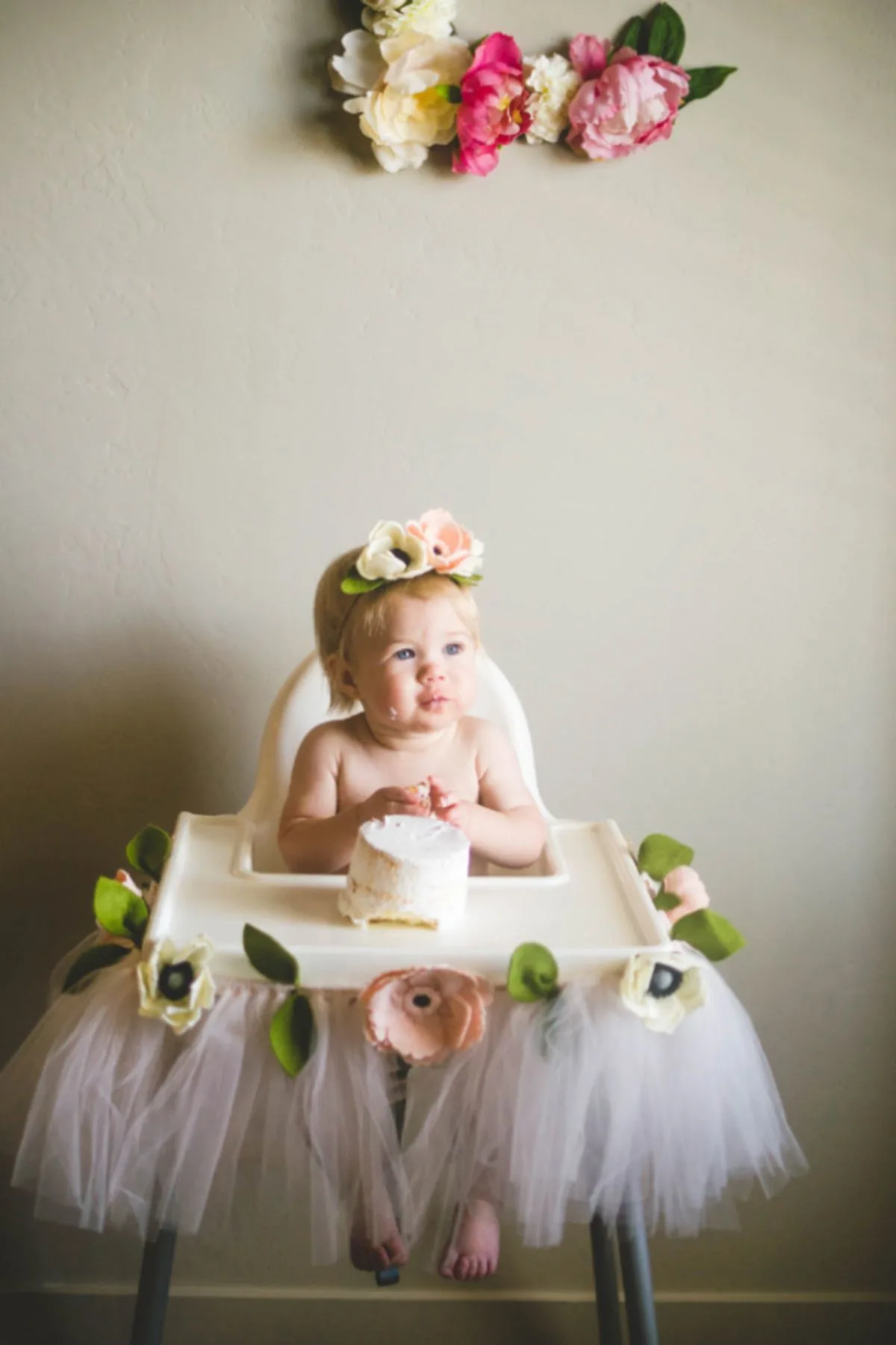 A little girl sits in her floral and tulle decorated high chair for her first birthday.