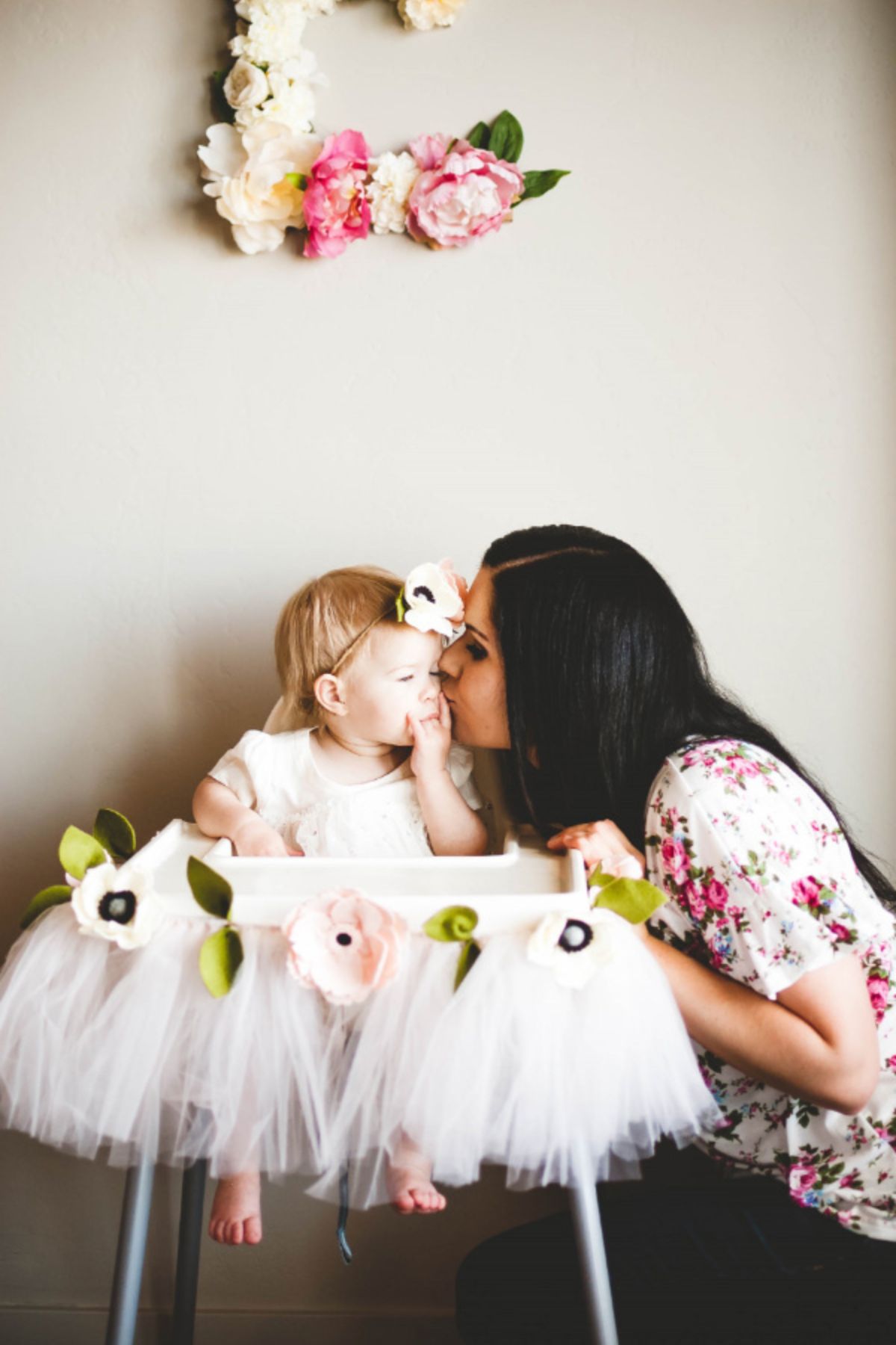 Mom kisses daughter during her floral first birthday party.