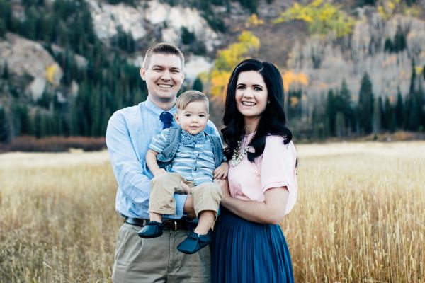 Man wearing blue shirt and tie and woman wearing pink shirt and teal skirt hold toddler boy during fall family photos.