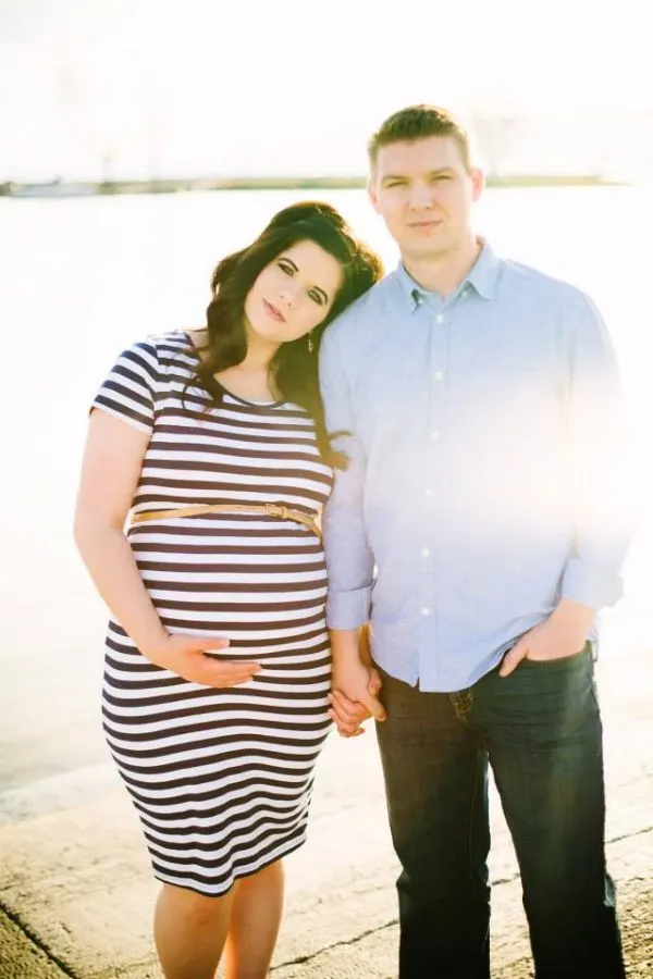 Woman wearing blue stripe dress leans head on man wearing blue shirt during maternity photos.