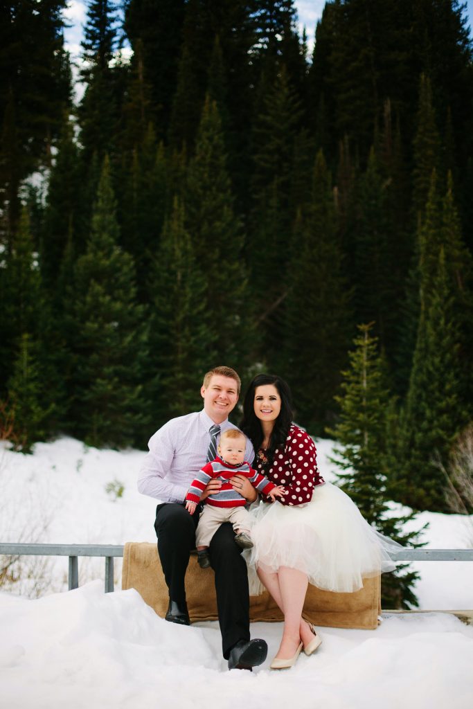 Family poses for family Christmas pictures in their winter outfits in snowy outdoor setting.