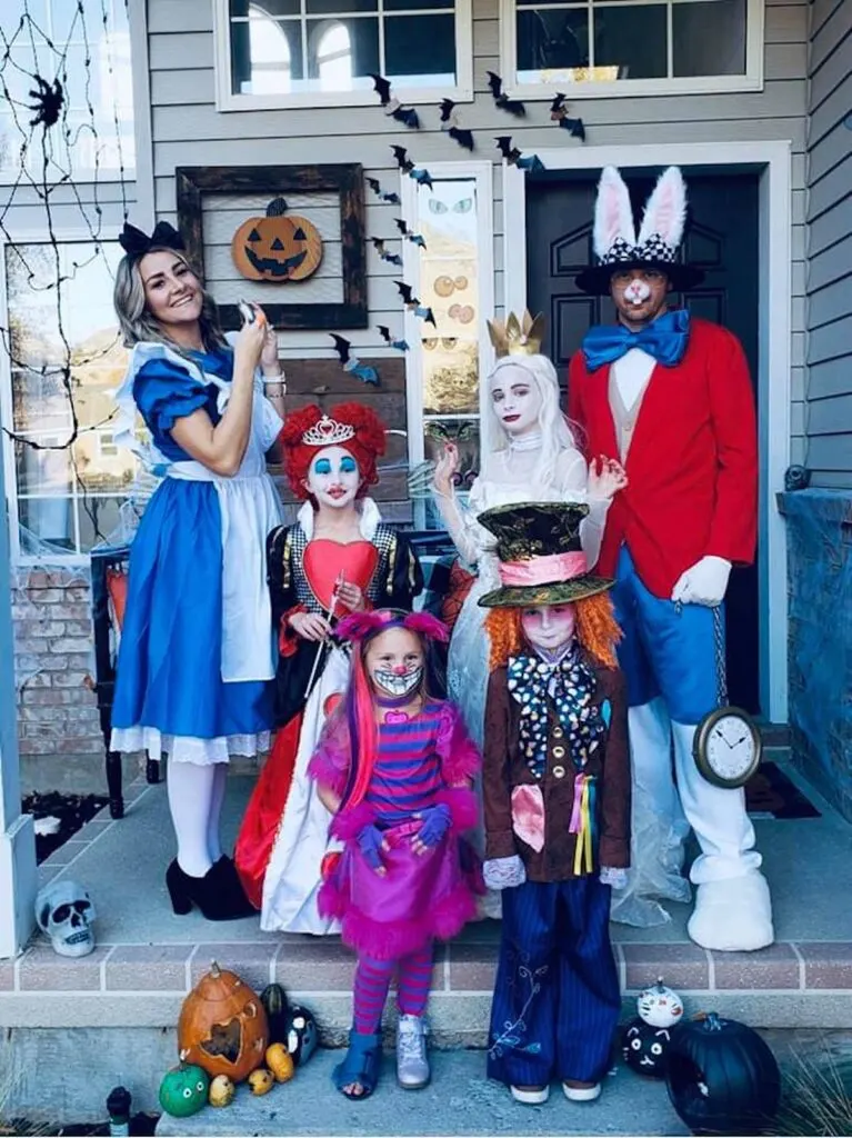 Family wearing Alice in Wonderland costumes stands on front porch and smiles.