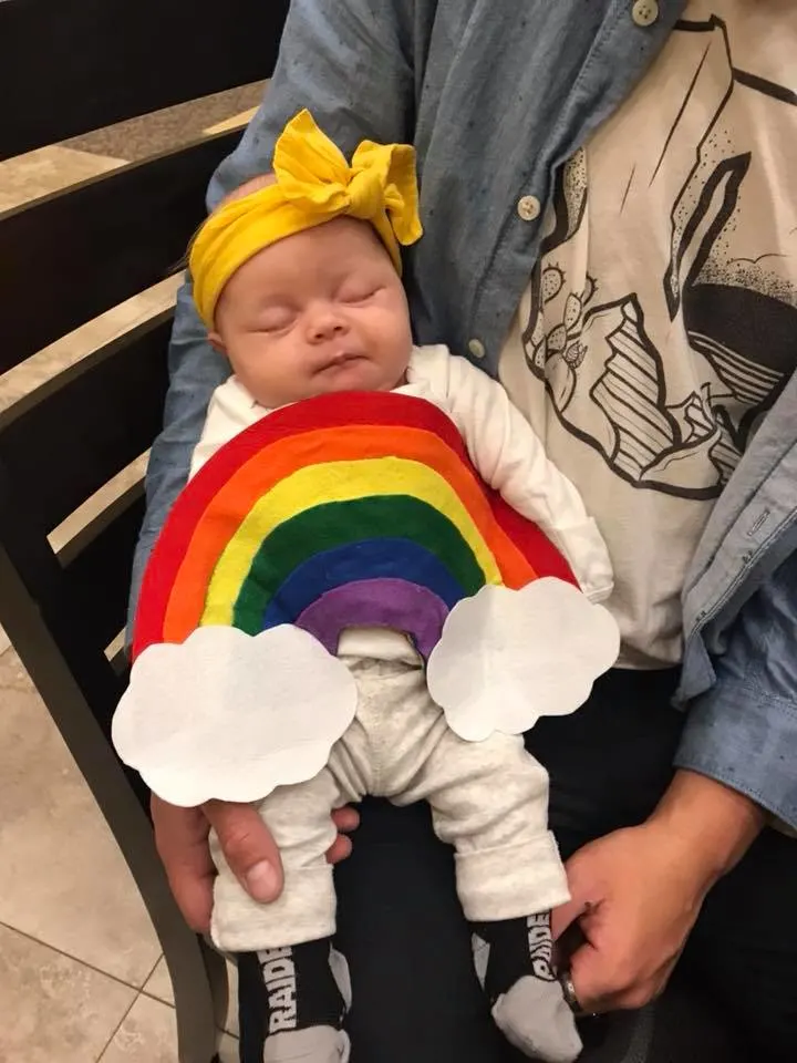 Baby wearing rainbow DIY baby Halloween costume sleeps in man's arms.