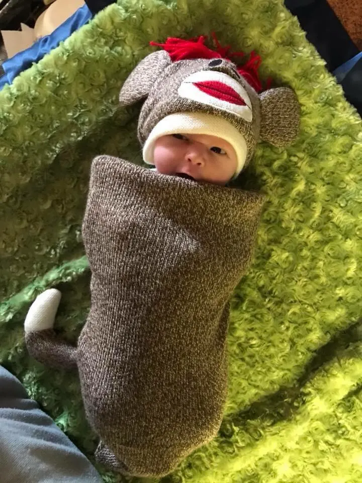Baby wearing sock monkey DIY baby Halloween costume lays on green blanket.