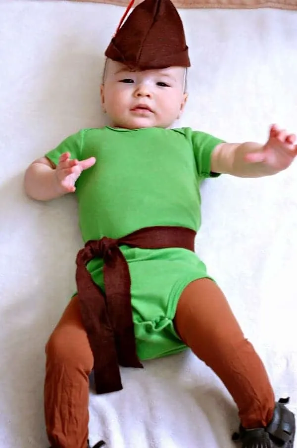 Baby boy dressed as Robin Hood lays on cream colored blanket.