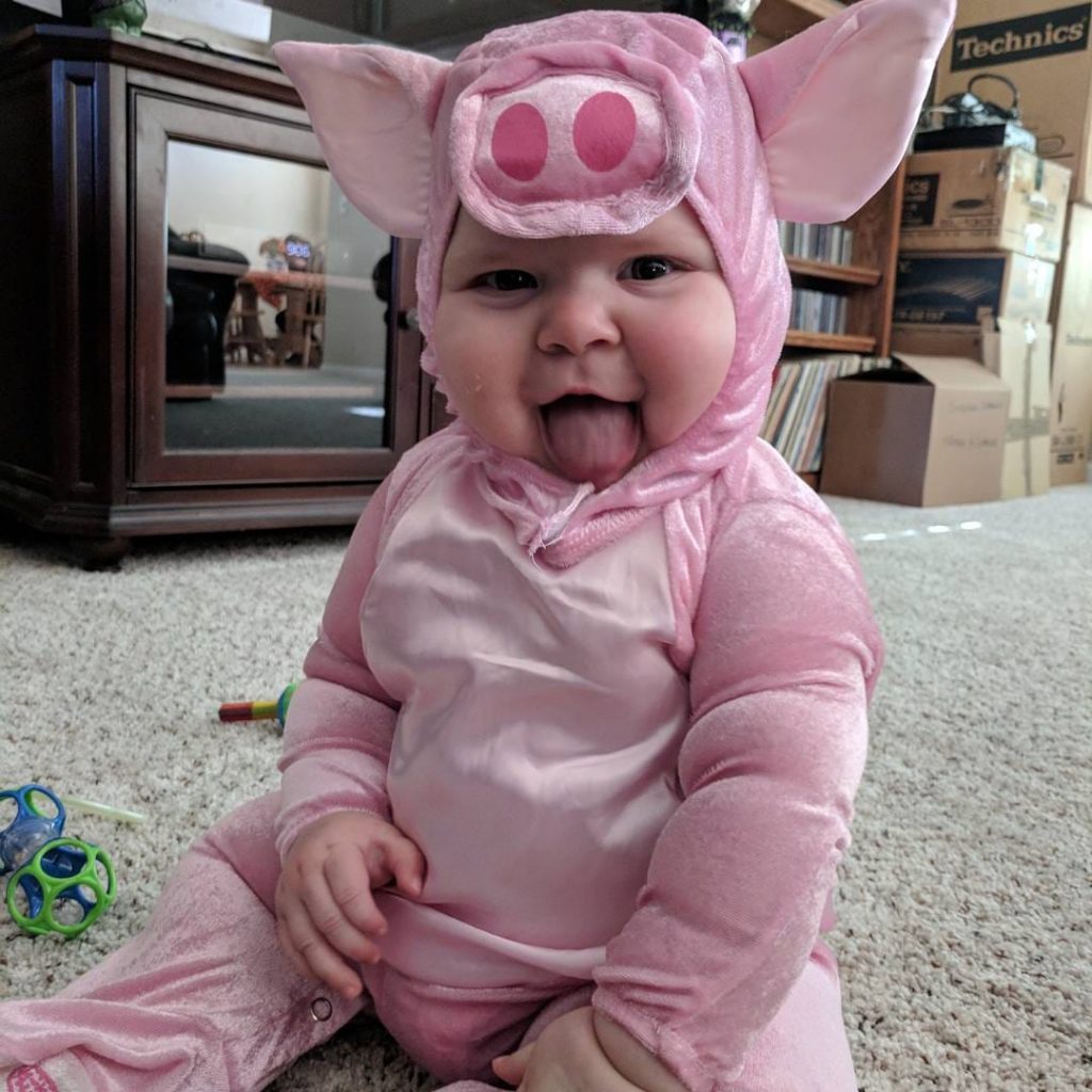 Baby sticks out tongue while wearing pink pig Halloween costume.