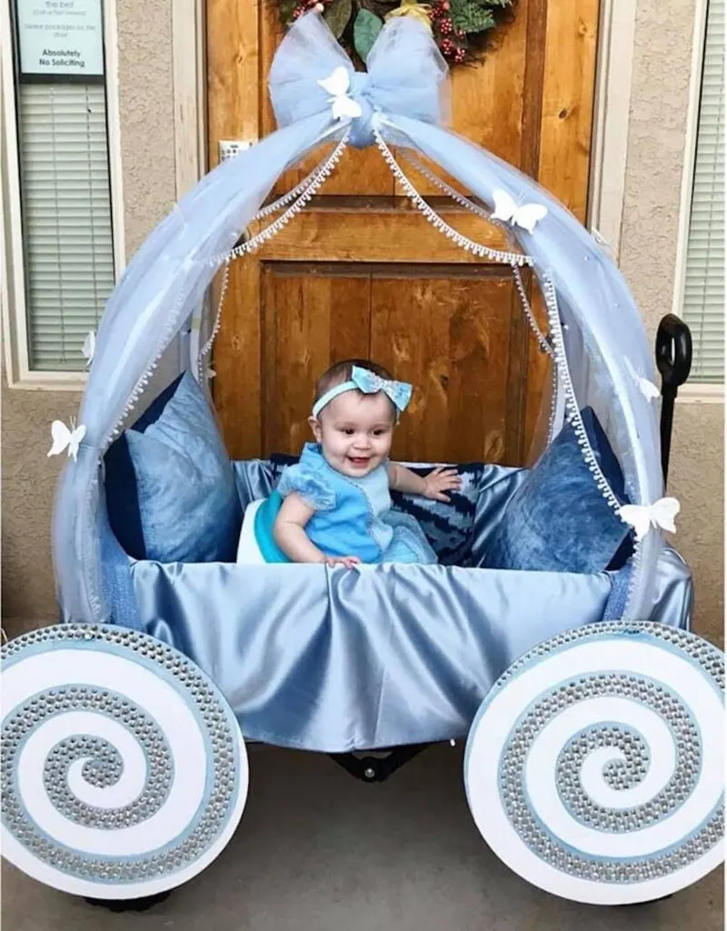 Baby girl wearing Cinderella costume sits in DIY carriage and smiles.