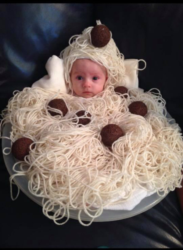 Baby wearing spaghetti and meatball DIY Halloween costume sits on blue couch.