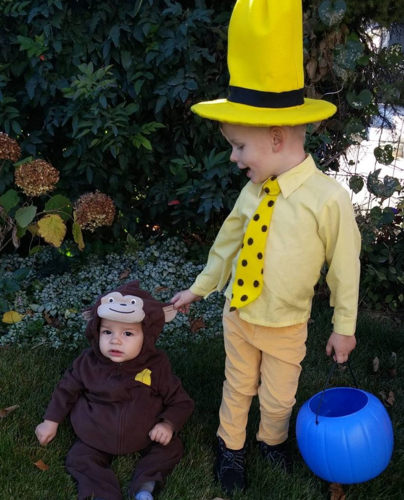 Boy wearing Man in the Yellow hat costume pulls on the ear of baby boy's Curious George costume.