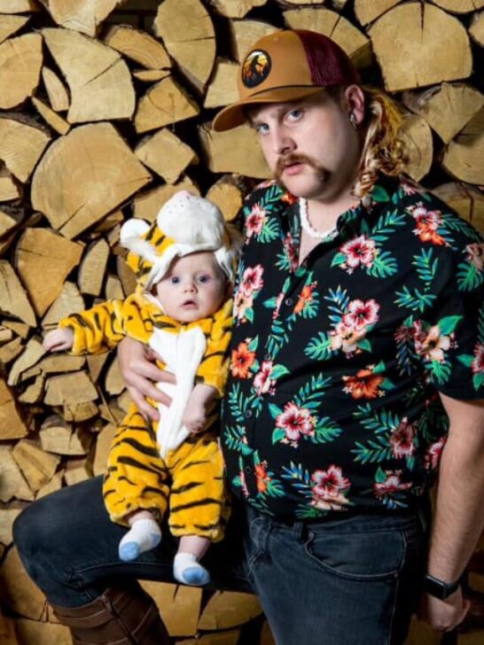 Man dressed as the Tiger King holds baby boy in tiger outfit.