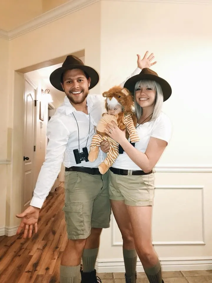 Family wearing safari Halloween costumes poses for picture near white wall.