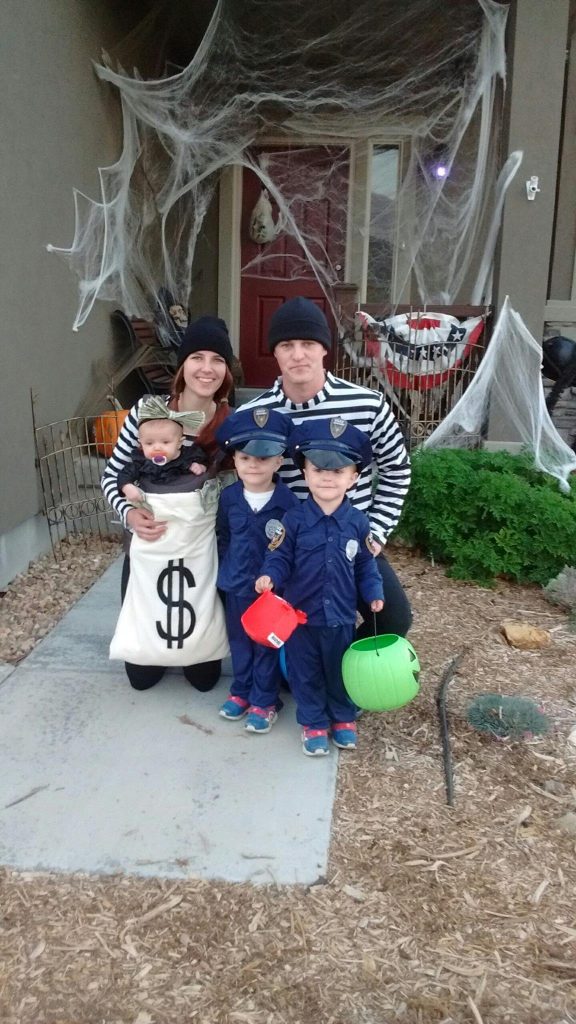Family wearing cops and robbers Halloween costumes stands in front of house for picture.
