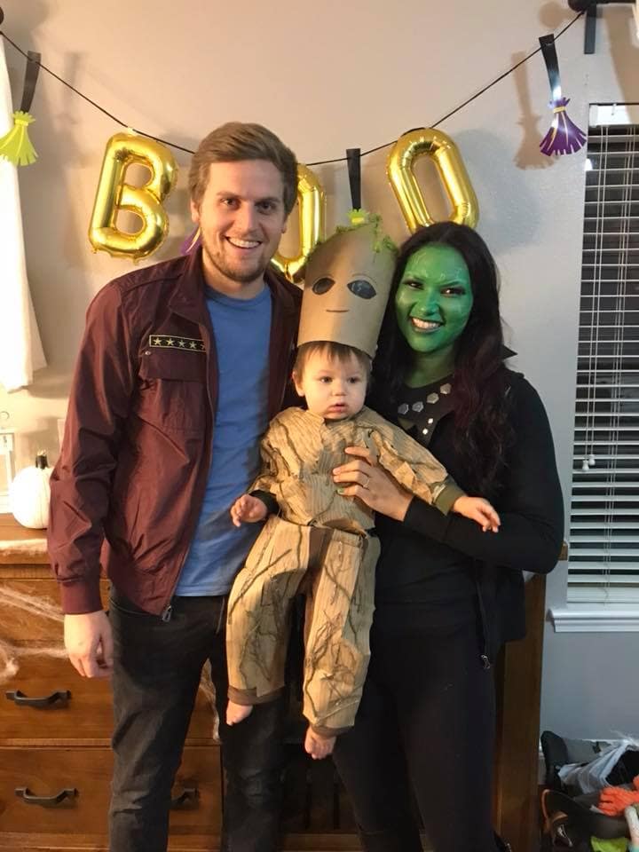 Family wearing Guardians of the Galaxy Halloween costumes smiles in front of decorations.