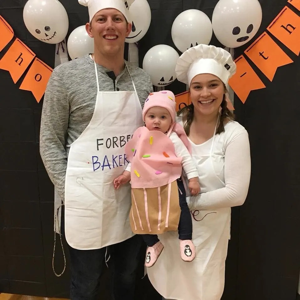 Family wearing baker costumes for Halloween smiles in front of holiday backdrop.