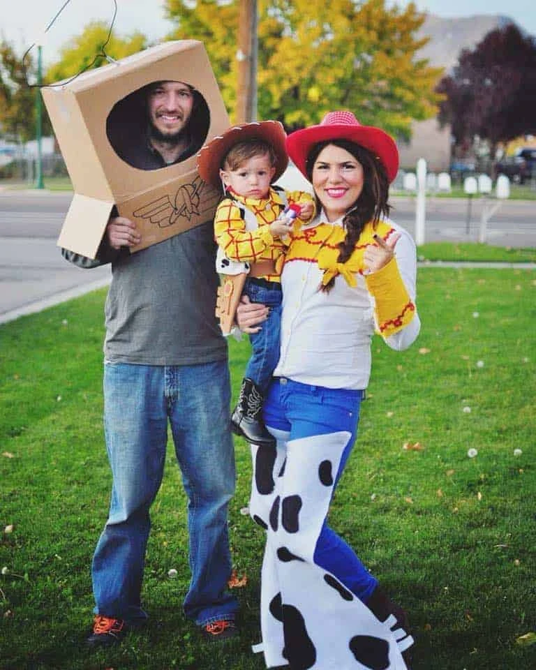 Family wearing Toy Story Halloween costumes smiles on lawn.