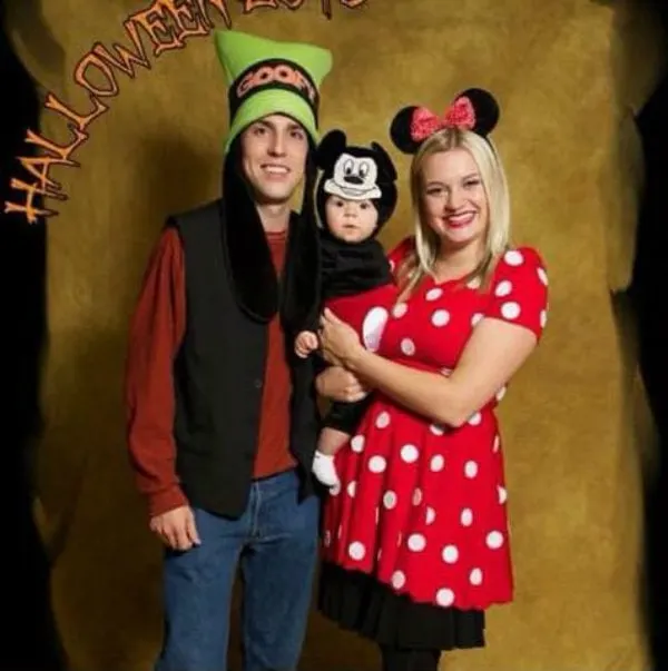Family wearing Mickey, Minnie, and Goofy costumes smile in front of photo backdrop.