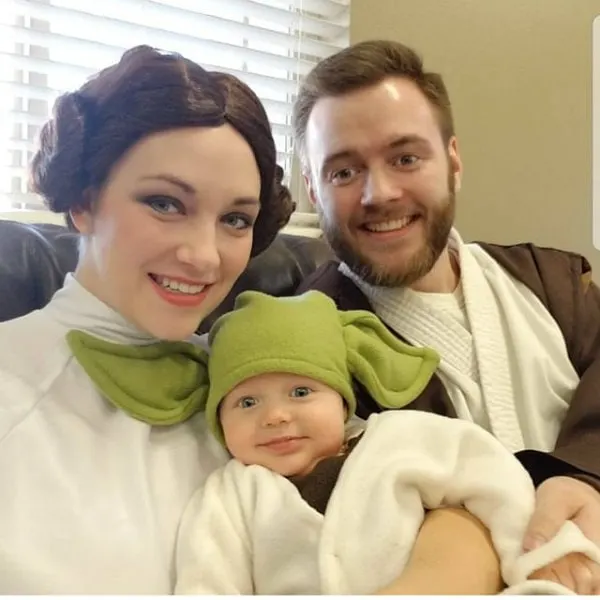 Man and woman wearing Star Wars costumes hold baby dressed up as Yoda.