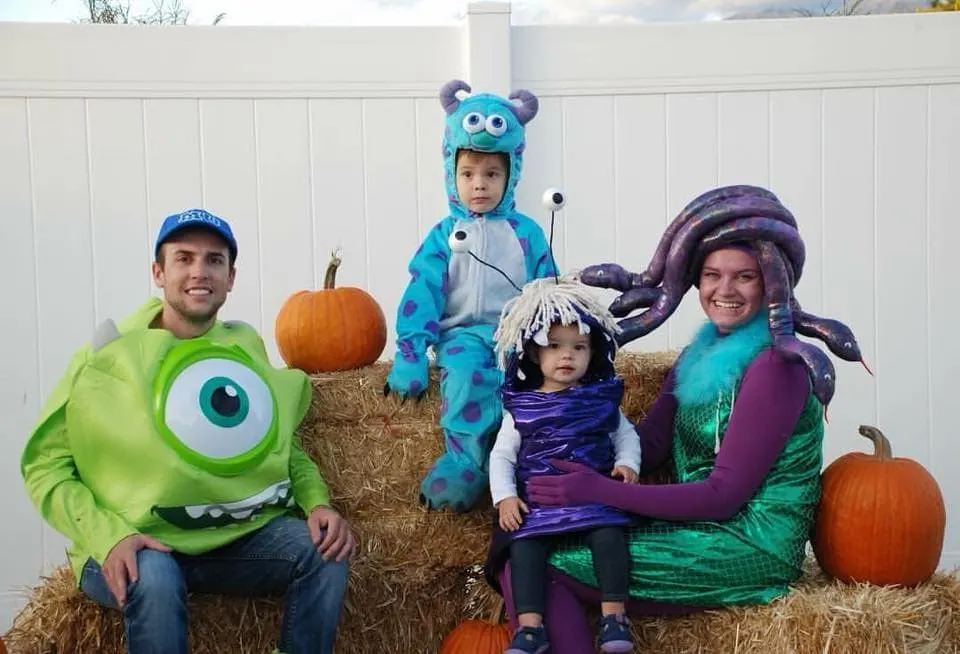 Family wearing Monsters Inc Halloween costumes sits on bales of hay and smiles.