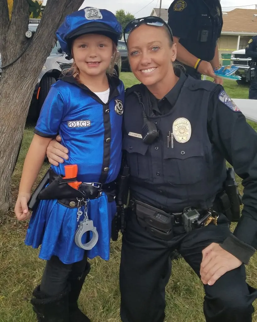 Girl wearing police kids Halloween costume hugs police officer.