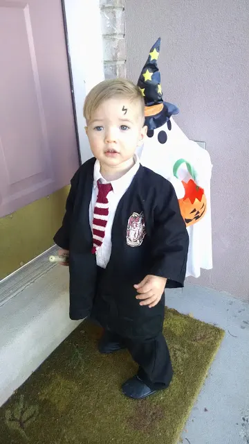 Baby boy wearing DIY Harry Potter Halloween costume stands on porch with decorations.