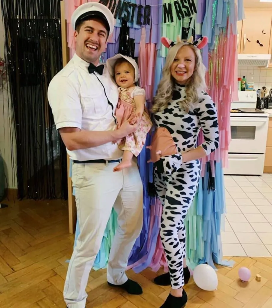 Man dressed as milk man holds baby girl next to pregnant woman wearing cow costume.