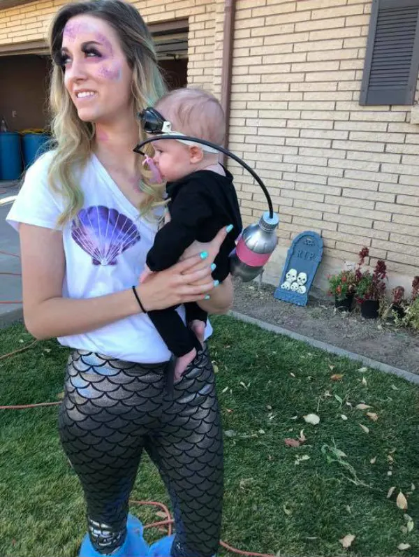 Woman wearing mermaid costume holds baby girl wearing scuba diver Halloween costume.
