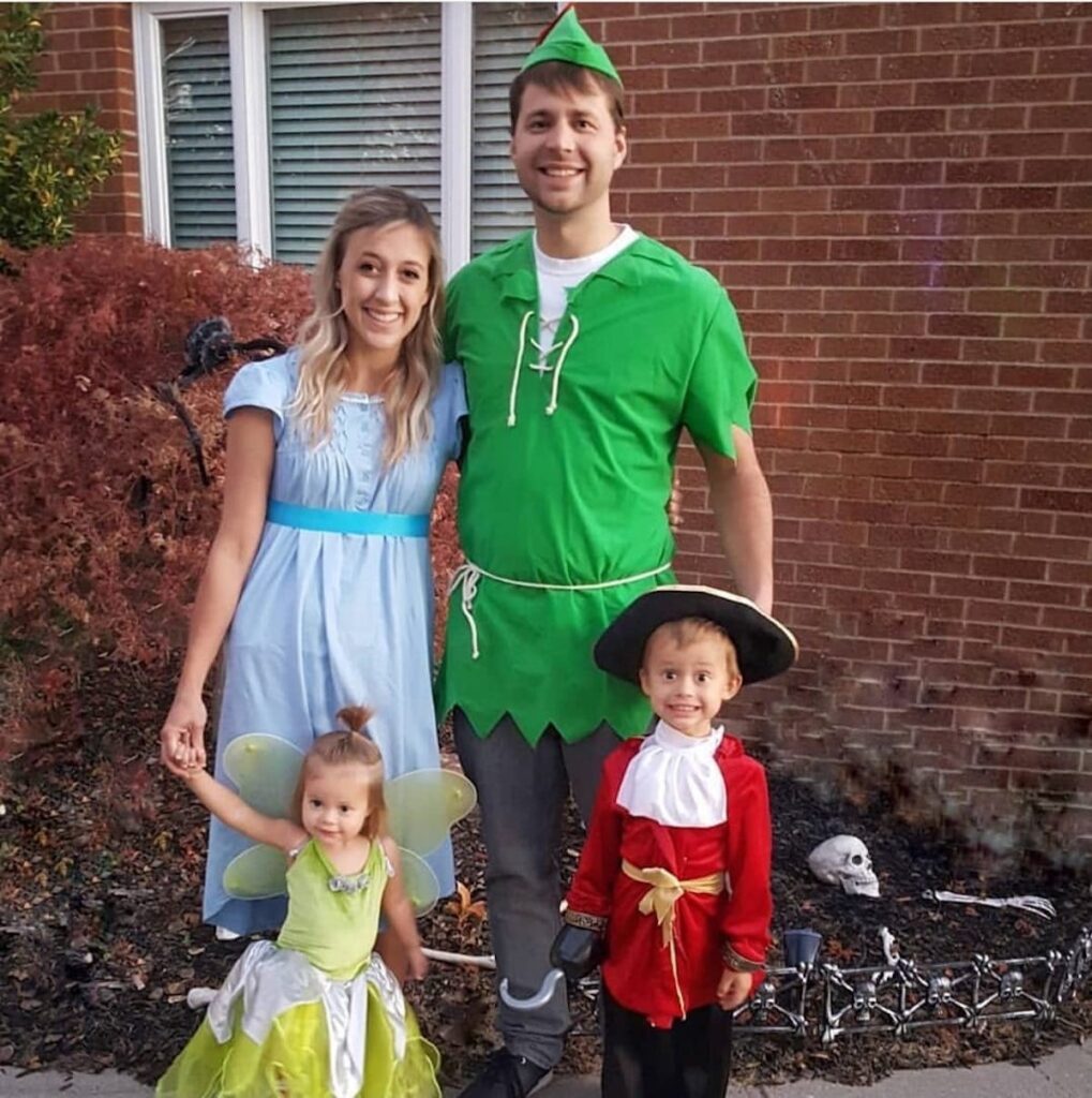 Family wearing Peter Pan character costumes smiles in front of red brick house.