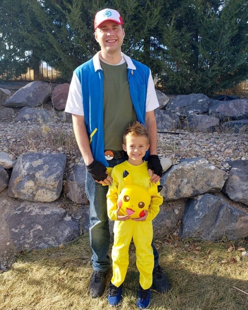 Man wearing Ash Ketchum costume stands behind boy wearing Pikachu costume.