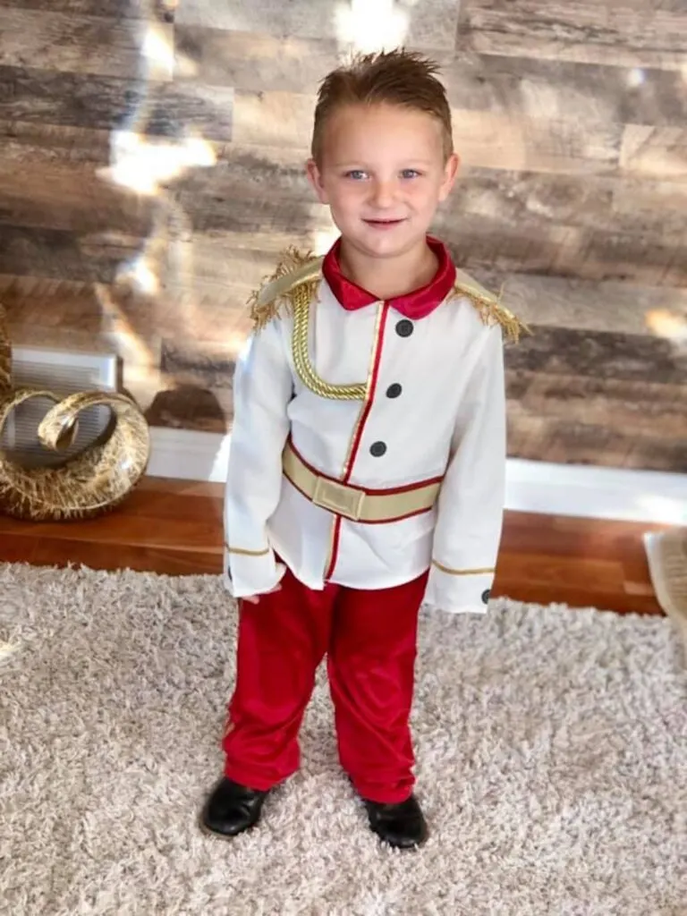 Boy wearing Prince Charming costume smiles in living room.