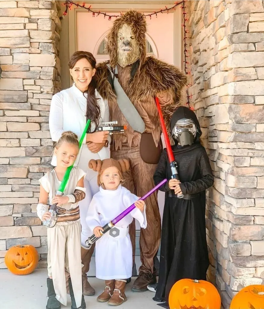 Family wearing Star Wars costumes smile on front porch with pumpkins.
