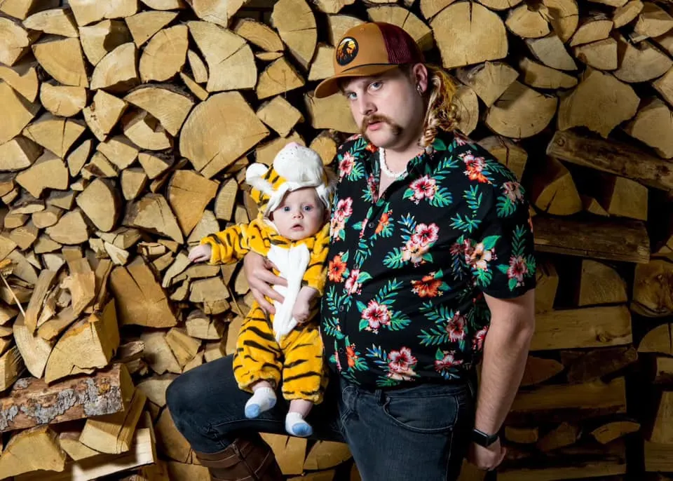 Man dressed as the Tiger King holds baby boy in tiger outfit.