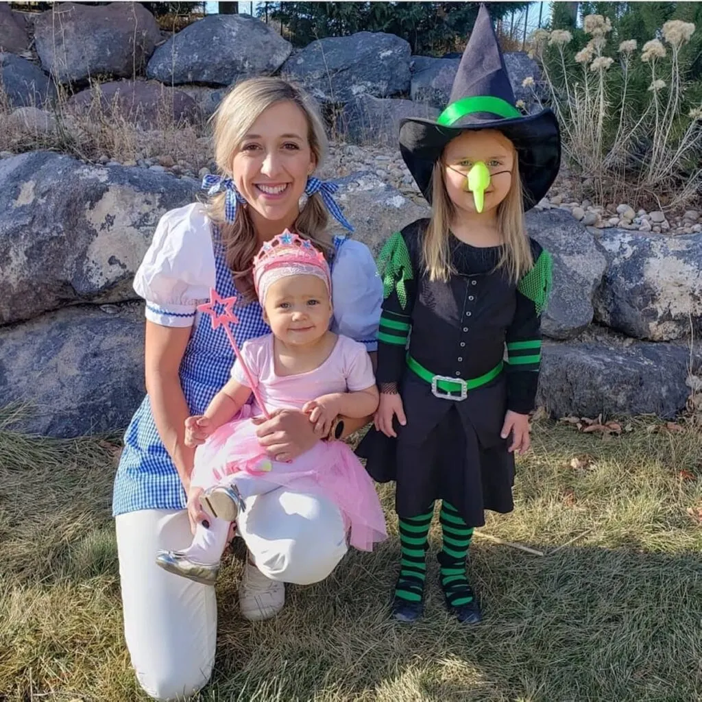 Woman and two girls wearing Wizard of Oz costumes smile in front of rock wall.