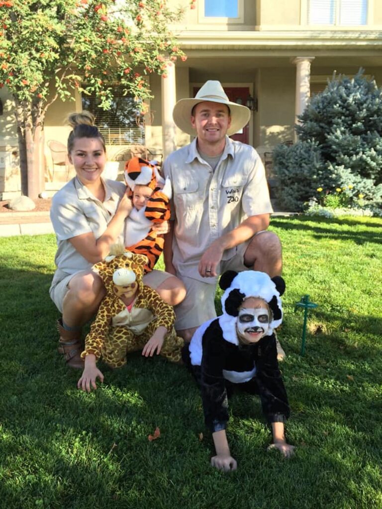 Family wearing zoo keeper and animal costumes smiles on front lawn.