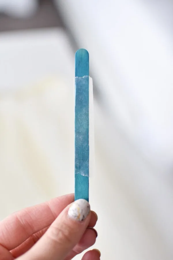 Woman holds blue popsicle stick with unwrapped fabric tape on it.