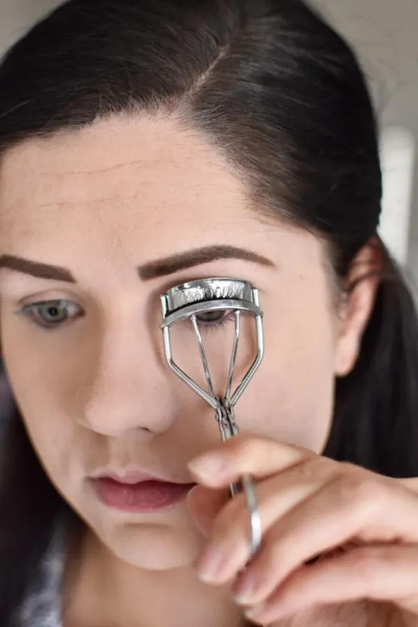 Woman curling eyelashes for a smokey eye tutorial 