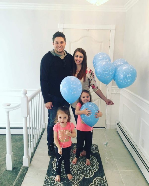 Family simles while holding blue balloons to announce baby's gender