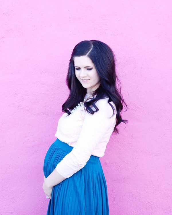 Pregnant mama holds her baby belly in front of pink wall.