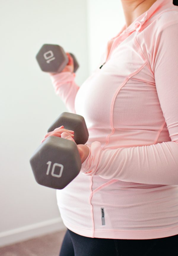 Woman holds dumbells during her exercise while pregnant.