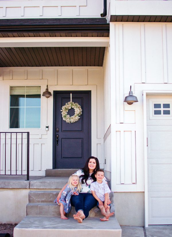 A young homeowner sits with her two kids in front of their new house.