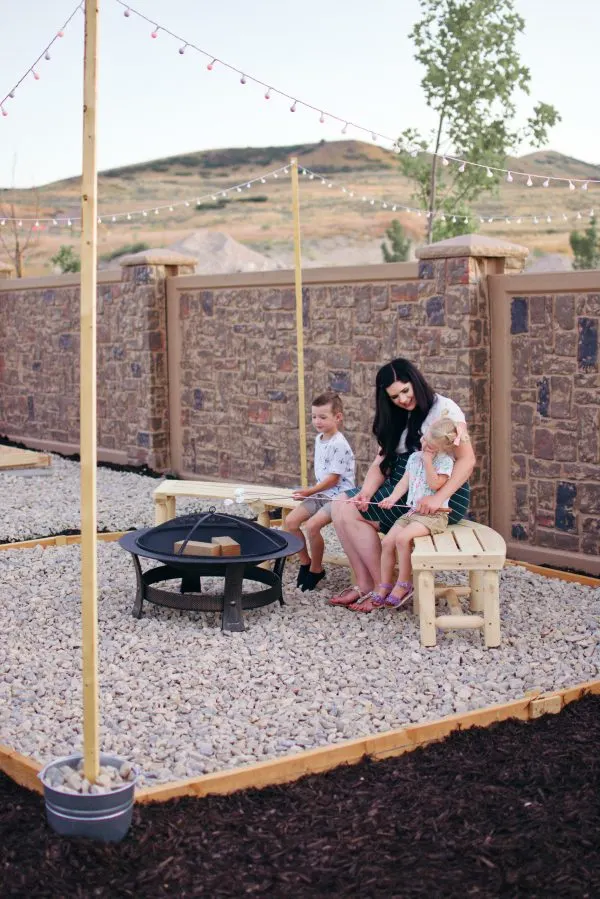 A mom and her two kids sit around their backyard fire pit.