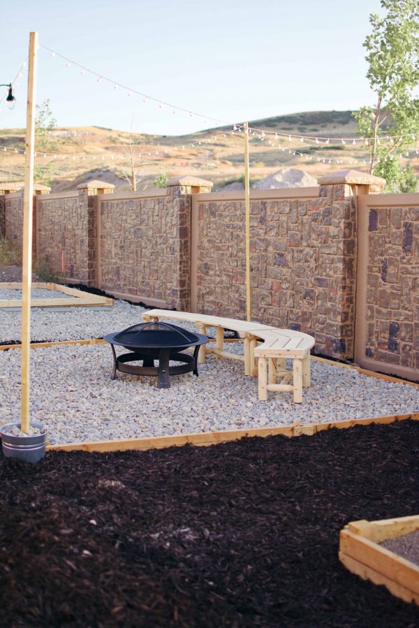Gravel fire pit area with black fire pit, wood benches, and wood light posts. 