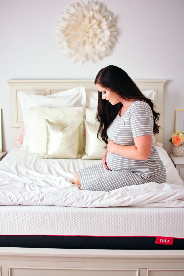 A woman sits on her tulo mattress and thinks about how to sleep while pregnant.