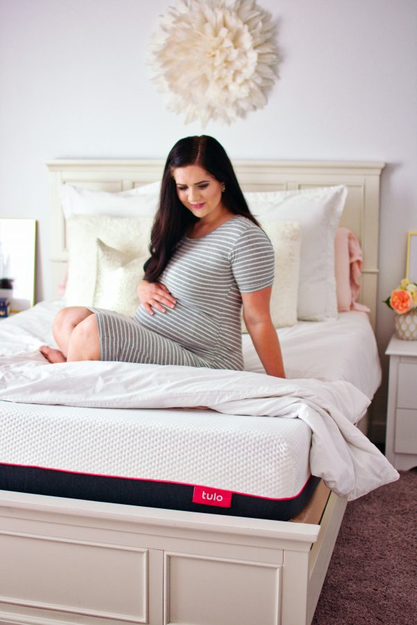 Mom holding baby bump and sitting on the best mattress for pregnancy.