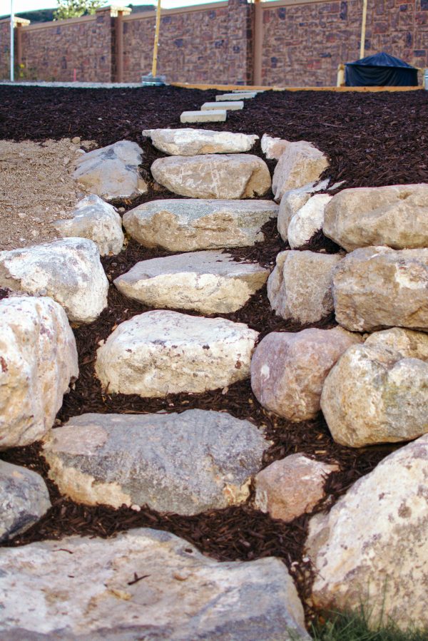 Rock steps in sloped backyard surrounded by brown mulch.