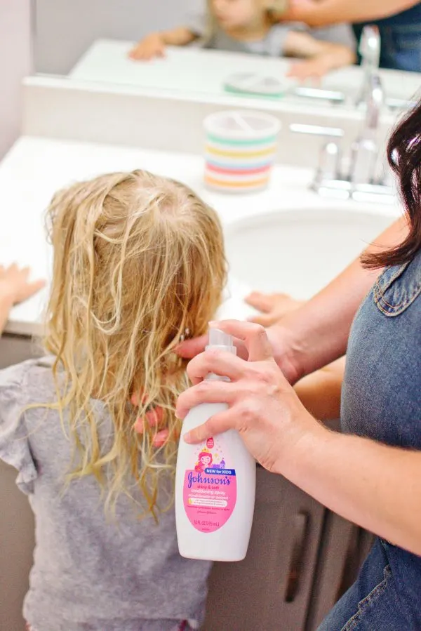 A mom shares hair tips and sprays Johnsons leave in conditioner for kids in her daughter's hair.