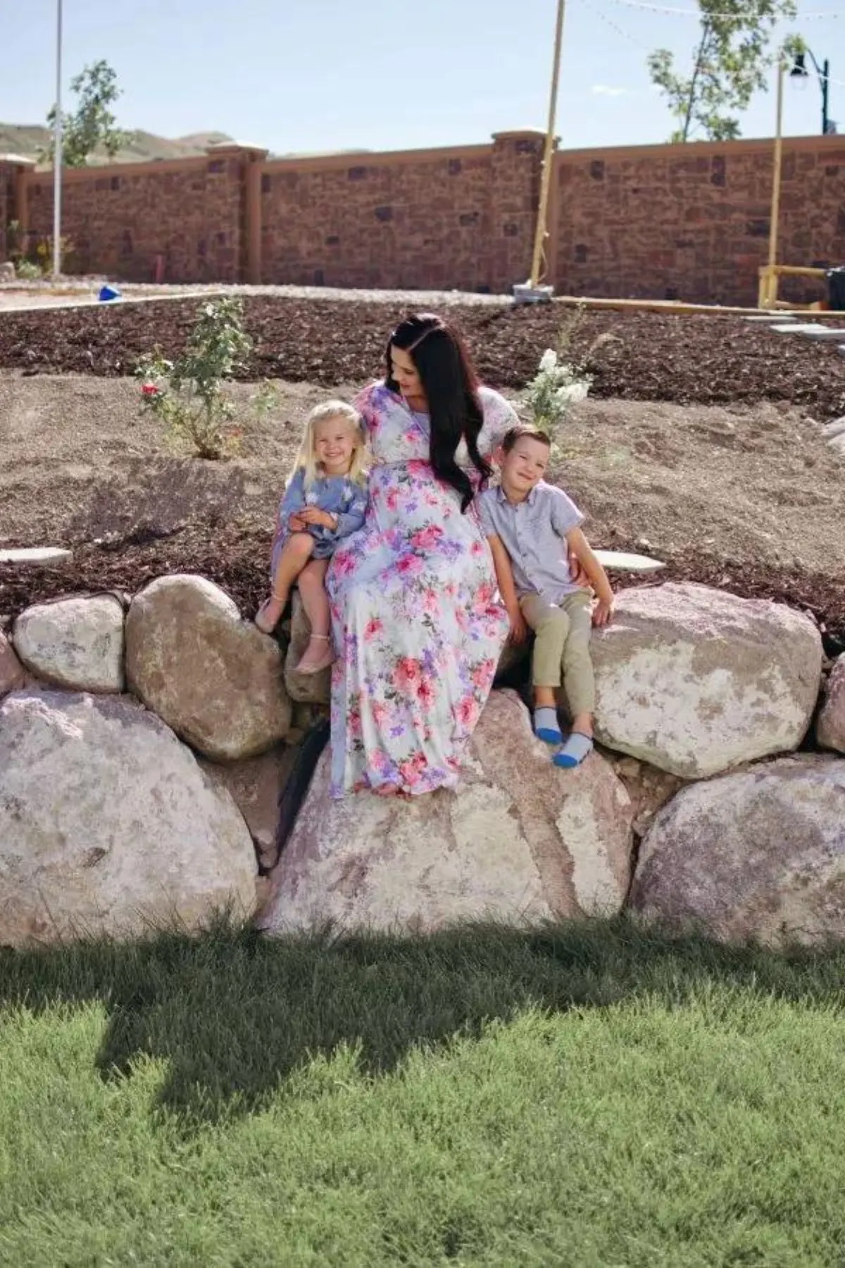 A mother sits with her children on large boulders in her backyard.