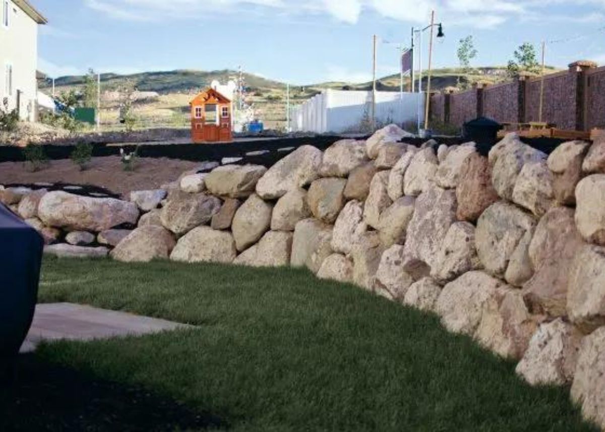 A backyard retaining wall made from large boulders and green grass.