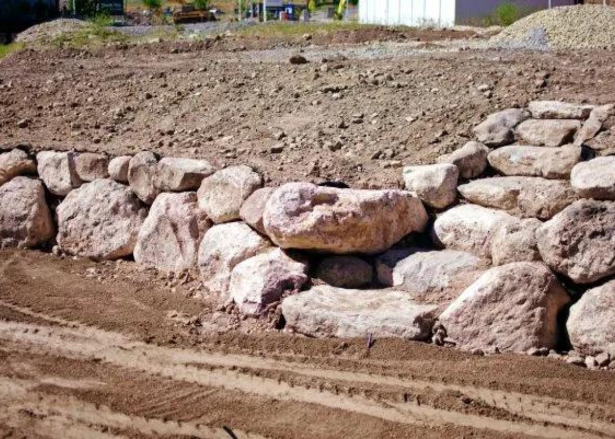 Unfinished dirt landscaping with large boulders to create a tiered backyard.