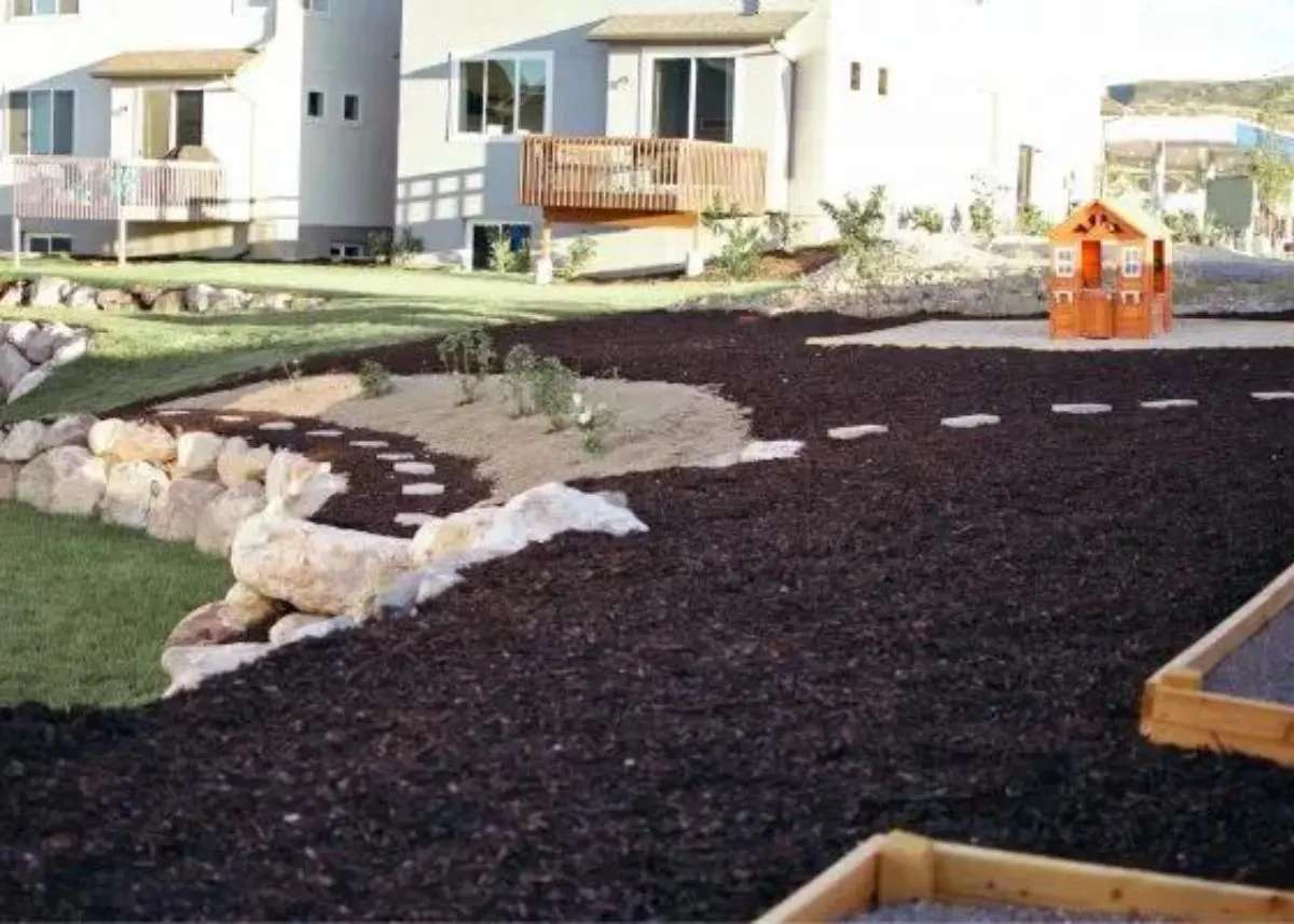 Dark mulch landscaping with stepping stones on the top tier of a sloped backyard.